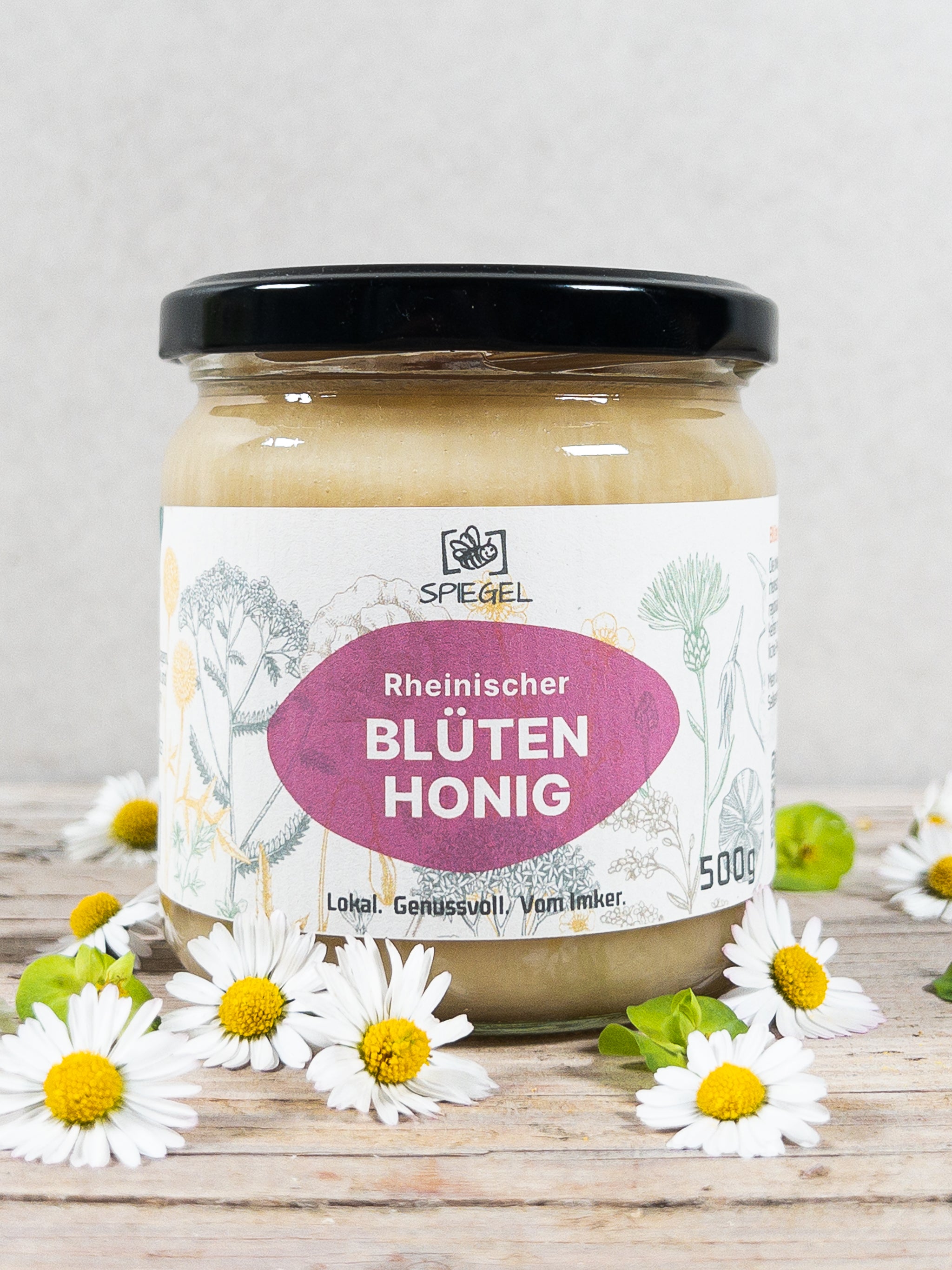 Glas Blütenhonig der Imkerei Silvester Spiegel, Rheinlad auf Holzplatte mit Gänseblümchen.