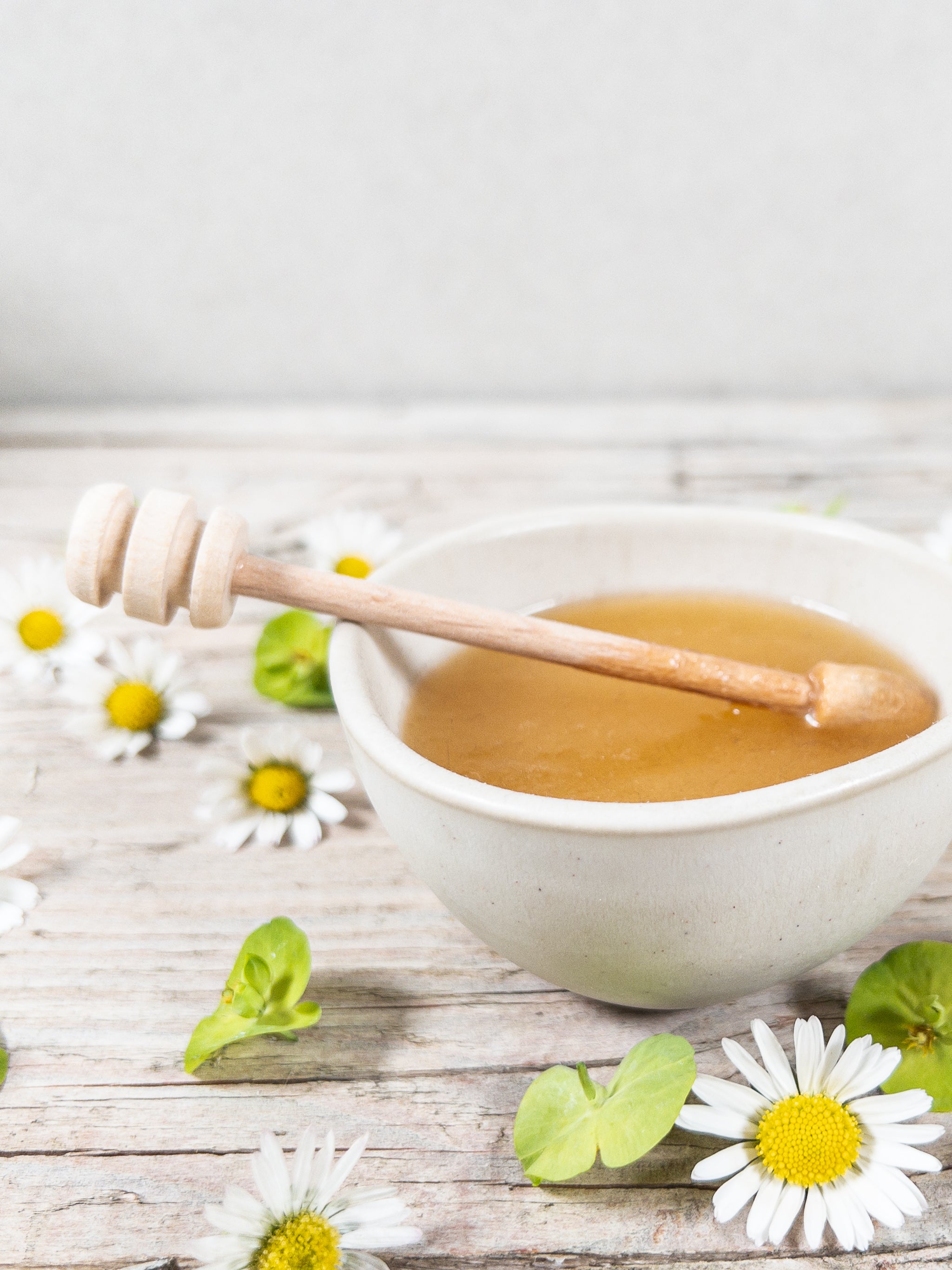 Blütenhonig in Steingut-Servierschale mit Holzlöffel und frischen Blüten.